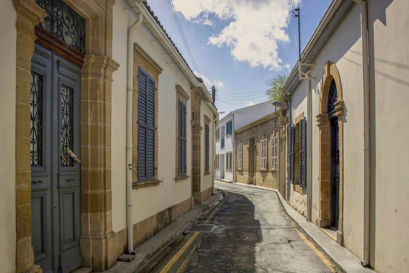 A narrow street of old houses with shuttered windows. A tall panelled door stands in the near wall.